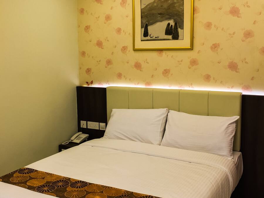 A hotel room with a bed, a nightstand with a phone, a wall with floral wallpaper, and a framed picture above the bed.