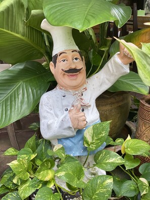 A ceramic chef figurine surrounded by large green leaves. - Khaolak Grand City (Takua Pa)