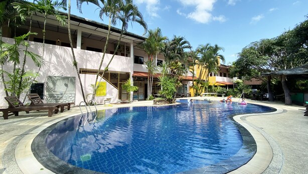 Una piscina con sillas de descanso y palmeras, rodeada de edificios.
