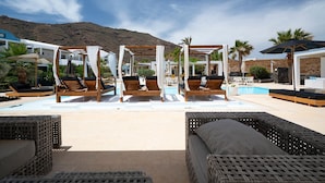 Zona de piscina con tumbonas de madera, una estructura con toldo y vistas a un paisaje montañoso.