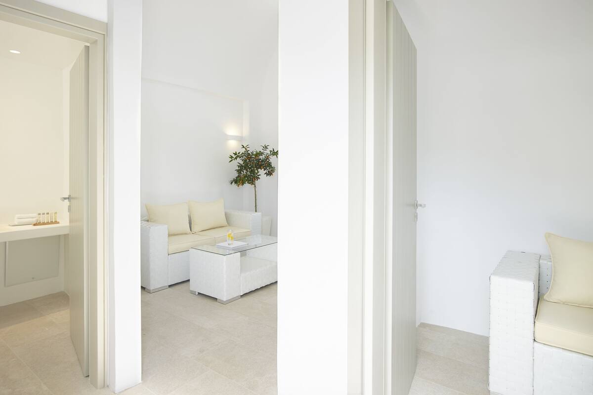 Une pièce moderne et minimaliste, avec un canapé blanc, une table basse en verre et une petite plante.