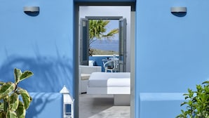 Una habitación moderna con una cama blanca, una mesita y vistas al mar a través de una puerta abierta.