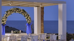 Decoración para una boda al aire libre con sillas blancas, un arco floral y faroles frente a un paisaje costero.