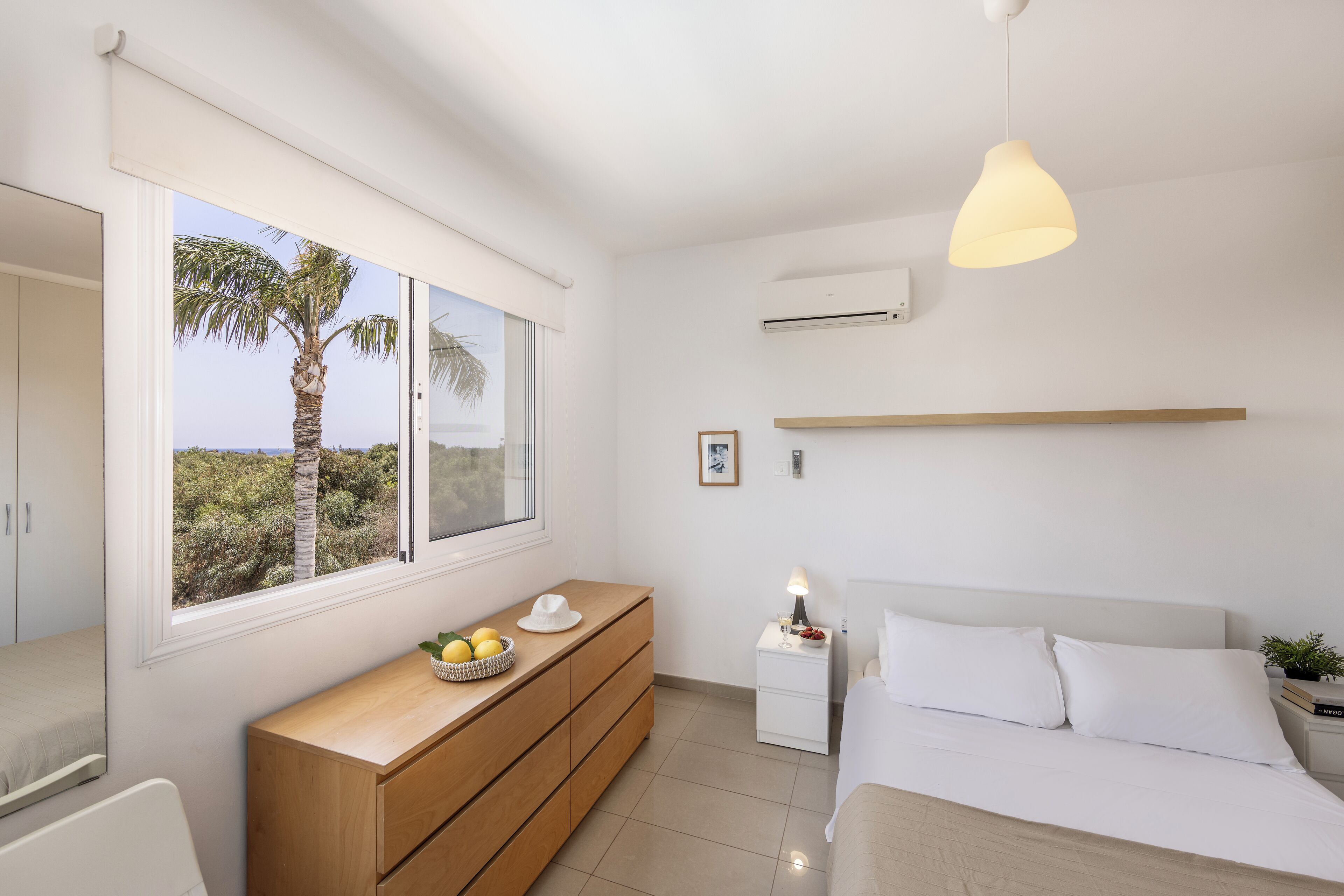 Un dormitorio con cama, mesita de noche, cómoda, ventana con vistas y una lámpara colgante.