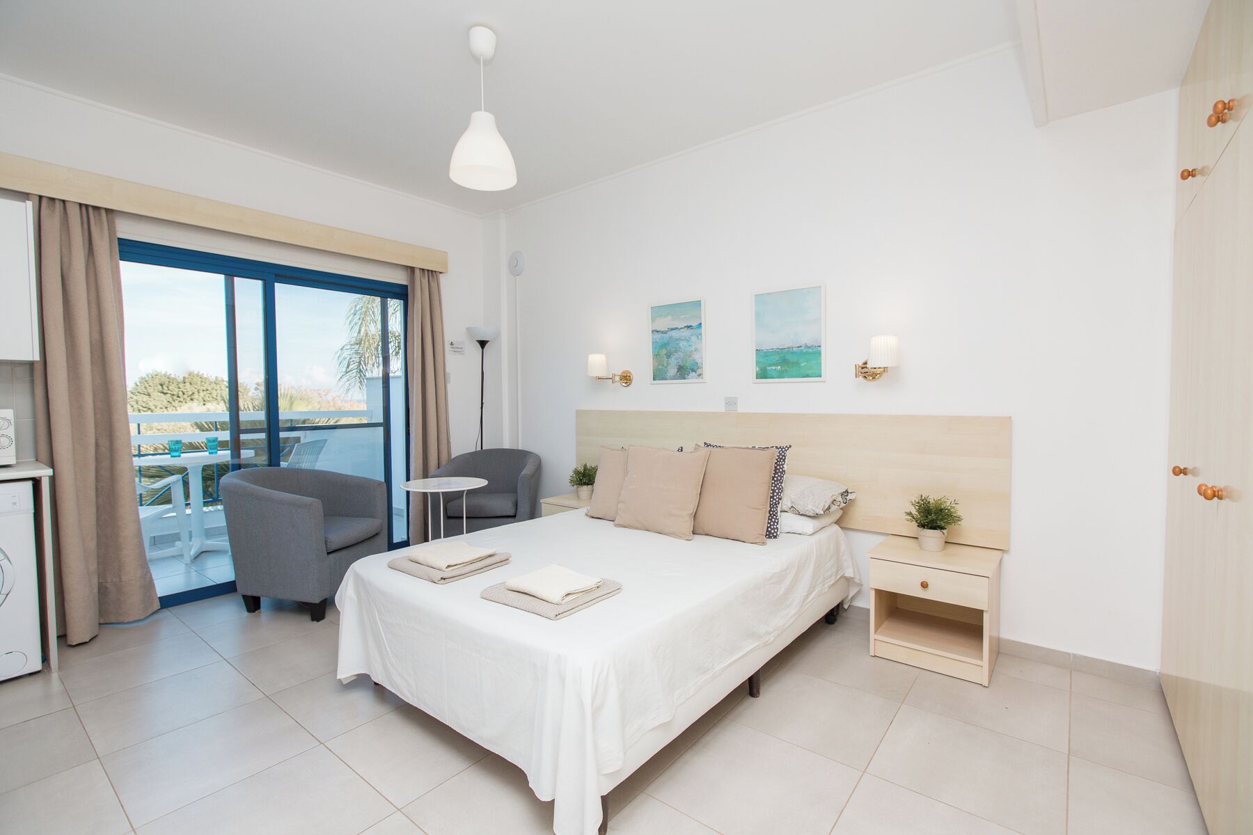 Quarto de hotel moderno com cama, mesa de cabeceira, cadeira e varanda com vista.