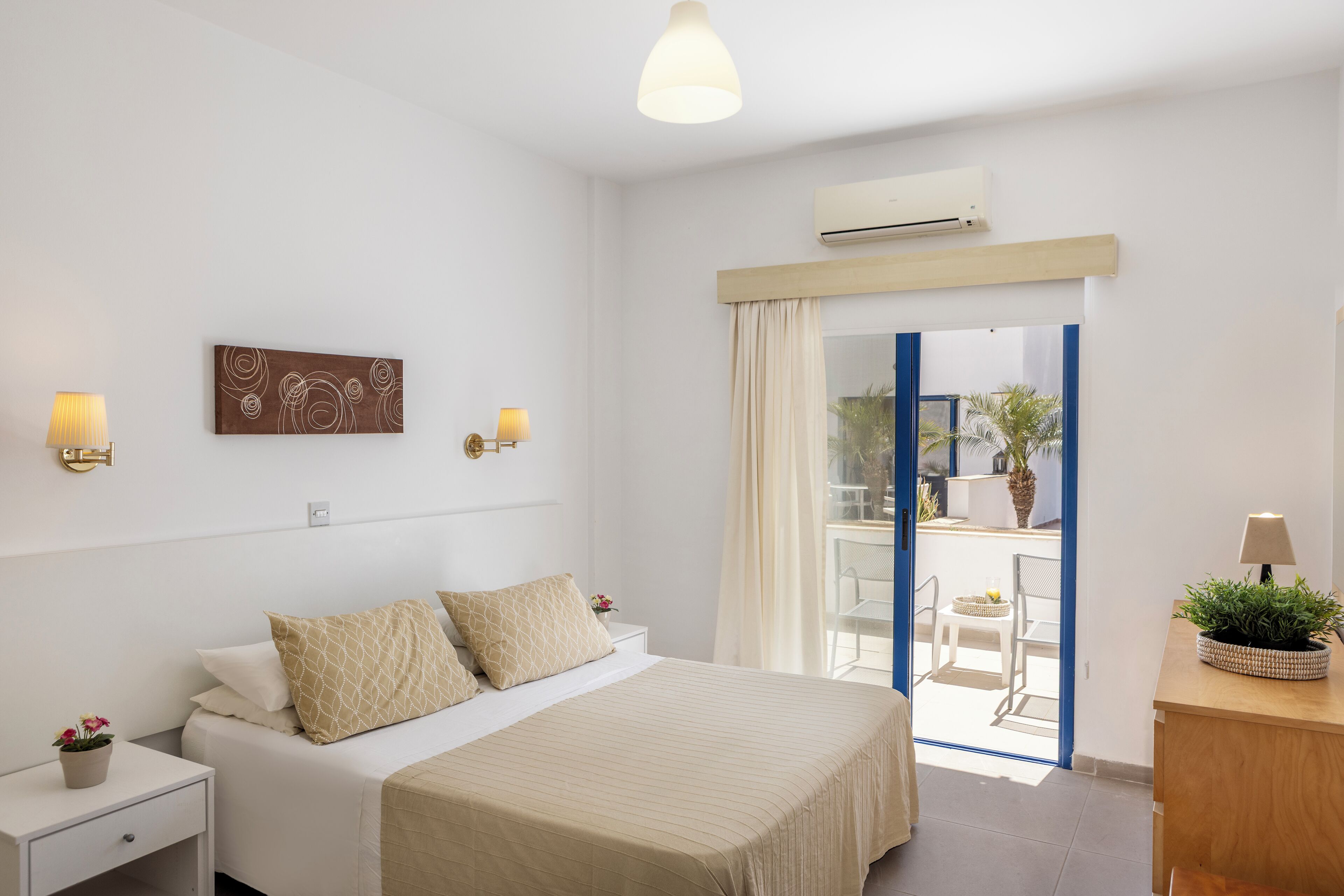 Habitación de hotel con cama, lámparas de noche, aire acondicionado de pared, ventana con cortinas y vistas al exterior.