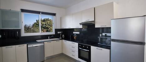 A modern kitchen with white cabinets, a dishwasher, an oven, a microwave, and a refrigerator.