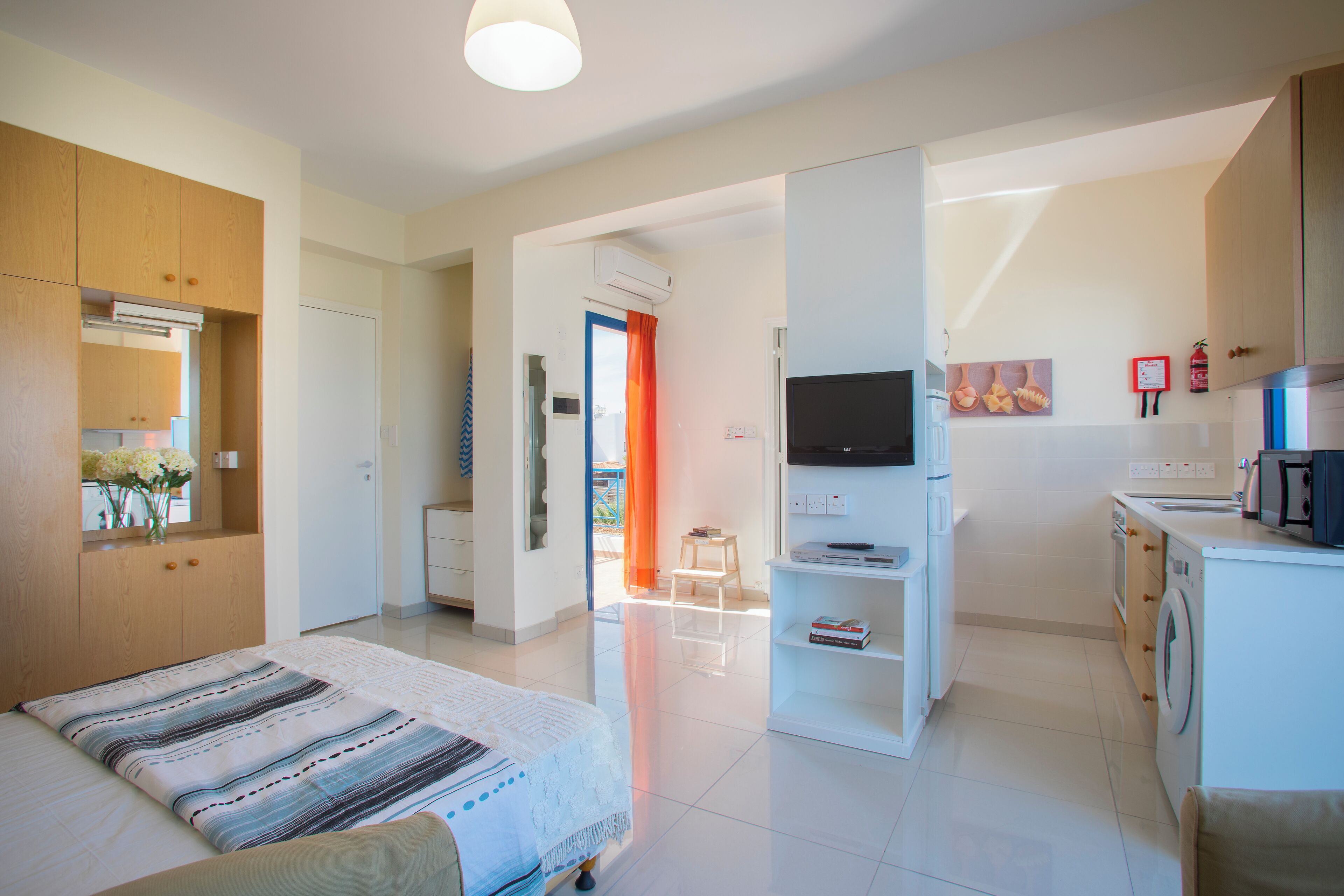 A modern hotel room with a bed, a TV, a small kitchenette, and a bathroom.