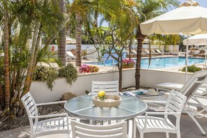 Un espace aménagé au bord de la piscine, avec des chaises longues blanches, une table ronde en verre et un parasol blanc.