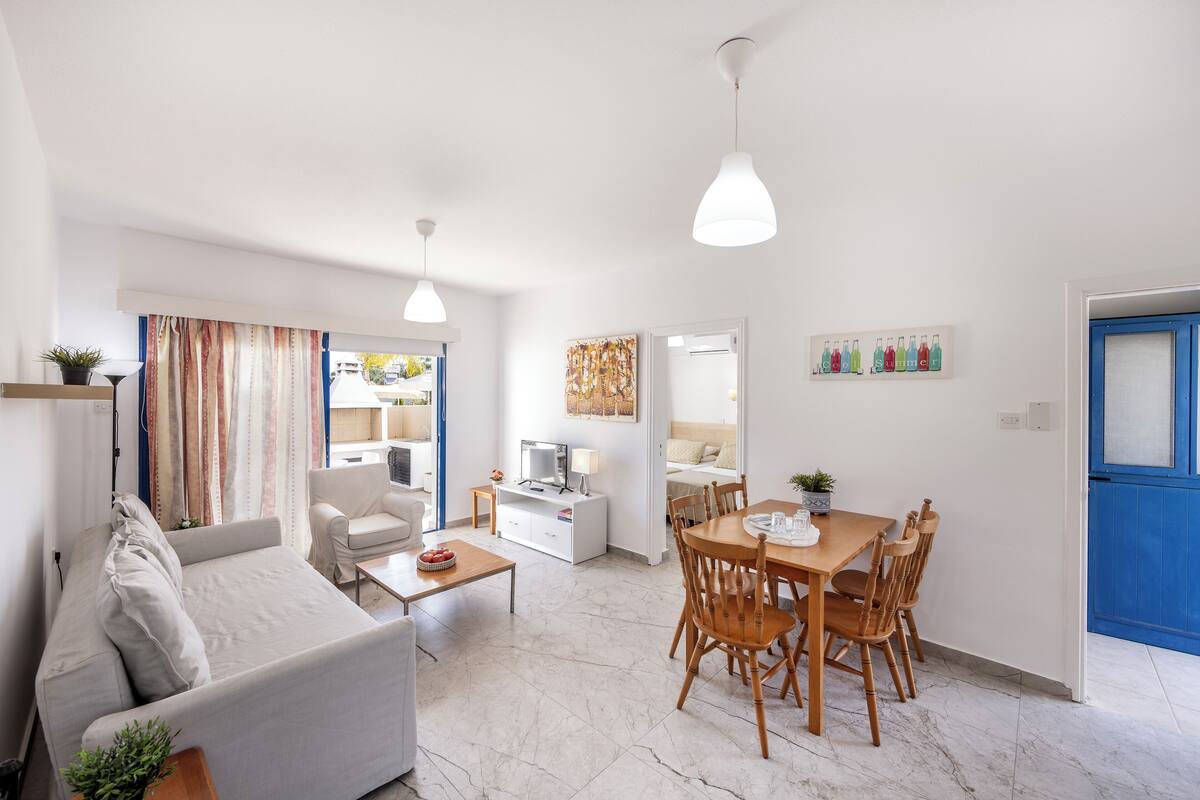 A modern living room with a sofa, coffee table, dining table with chairs, and a TV.
