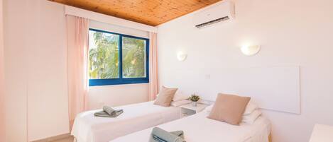 Habitación de hotel con dos camas, techo de madera y ventana con vista a palmeras.