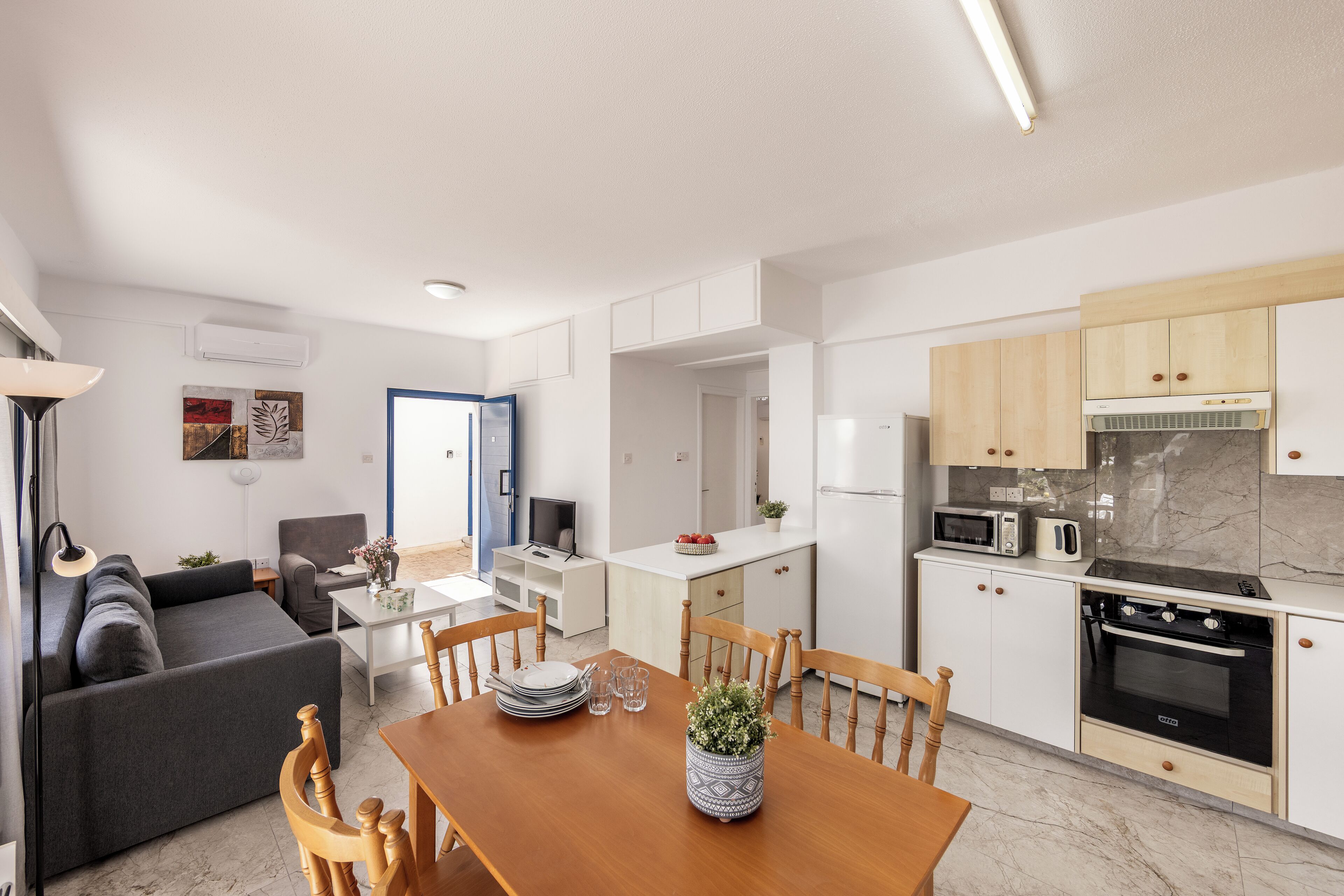 A modern kitchen with white cabinets, a built-in oven, and a dining area with a wooden table and chairs.
