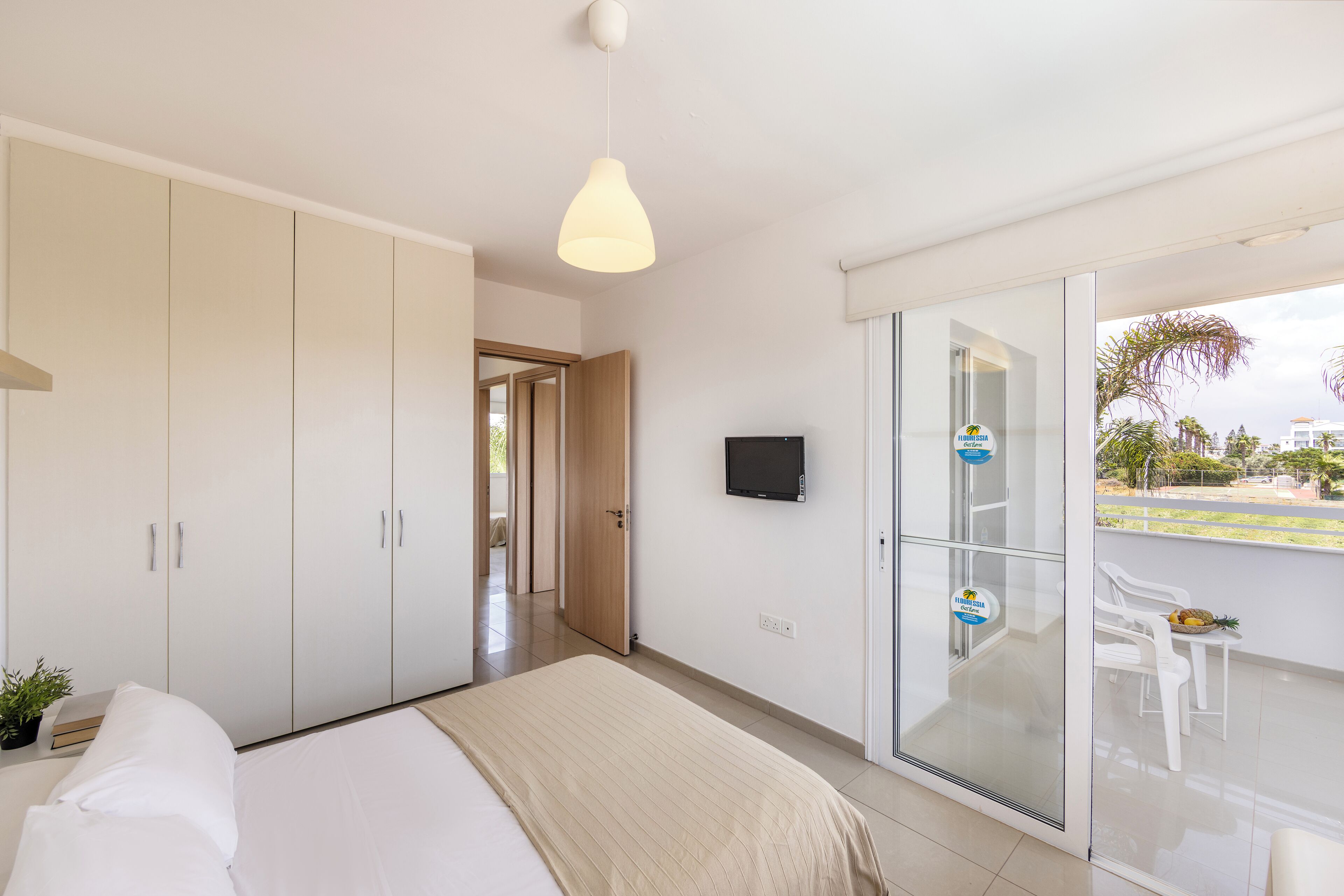 A bedroom with a bed, a TV, a balcony with chairs, and a view of the outside.