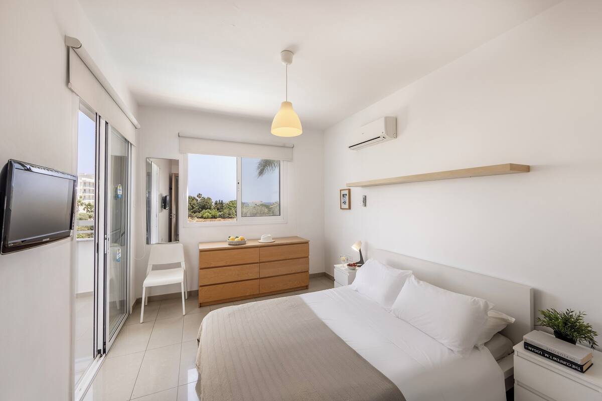 A modern bedroom with a bed, bedside table, and a TV mounted on the wall.