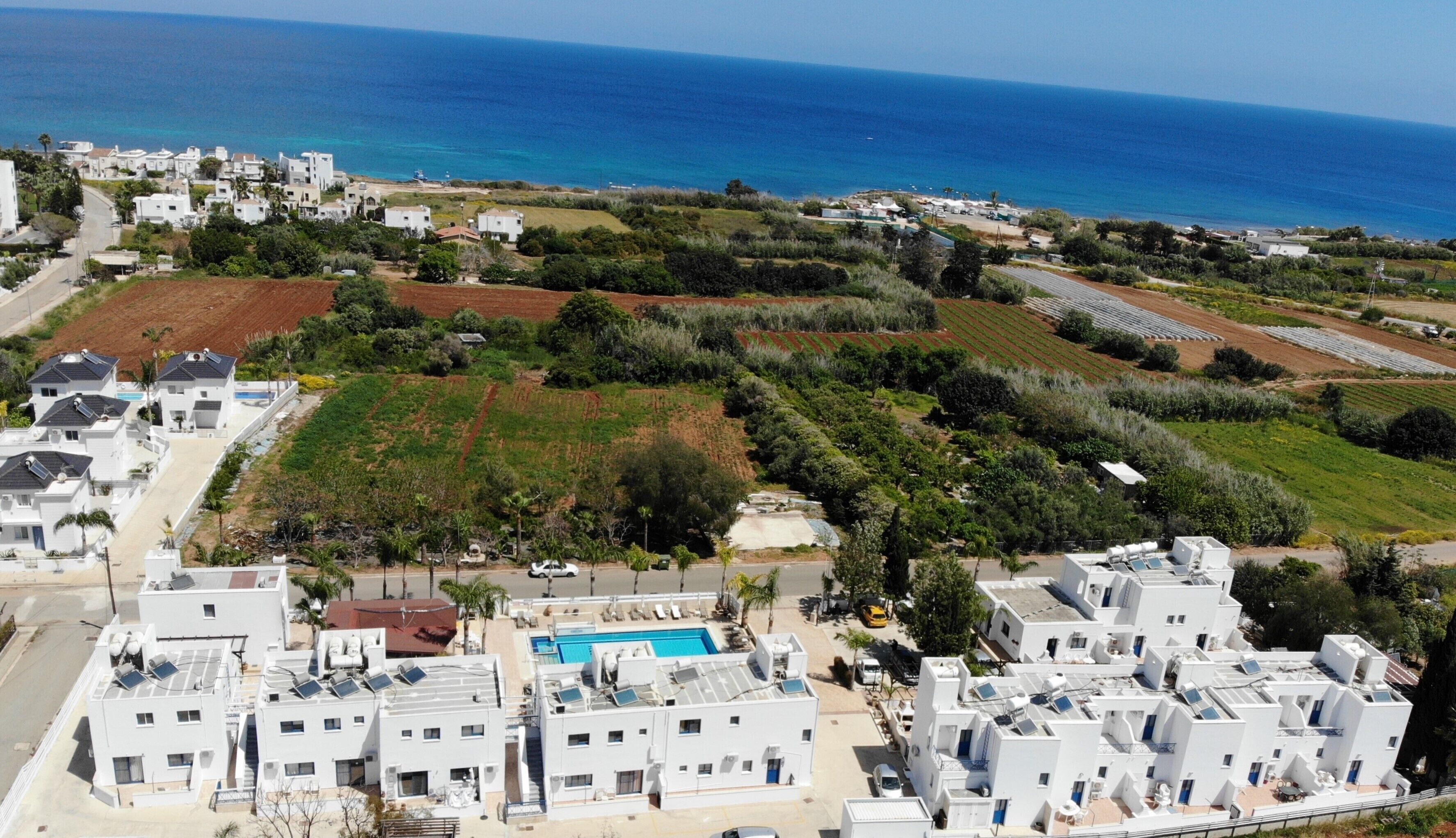 A coastal residential area with white buildings, a swimming pool, and a view of the sea.