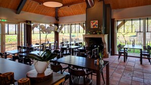 A restaurant with wooden ceilings, large windows, and a fireplace. Tables and chairs are arranged for dining. - Hotel Hof van 's Gravenmoer (Gravenmoer)