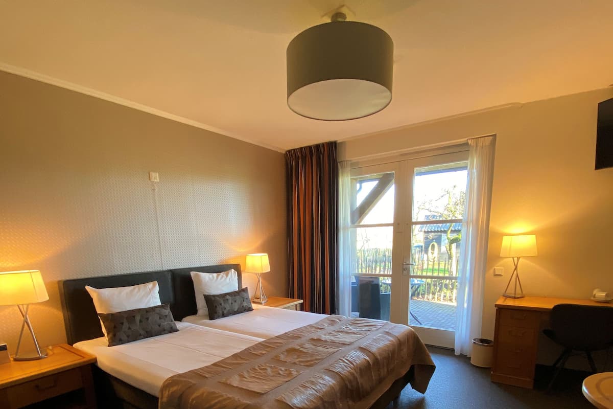 Une chambre d’hôtel avec un grand lit, deux tables de chevet avec des lampes, un bureau avec une chaise et une vue sur l’extérieur par une fenêtre.