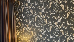 A hotel room with a large bed, two pillows, a nightstand with a lamp, and a dark wall with floral wallpaper. - Hotel Hof van 's Gravenmoer (Gravenmoer)