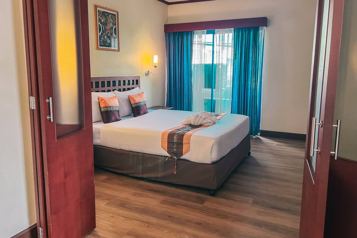 A hotel room with a large bed, a nightstand, a wall-mounted lamp, and a window with curtains.