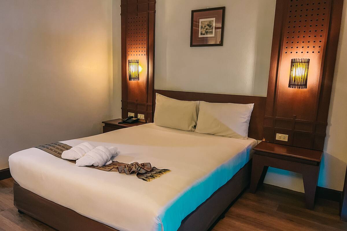 A hotel room with a large bed, wooden headboard, two bedside tables, a telephone, and wall-mounted lights.