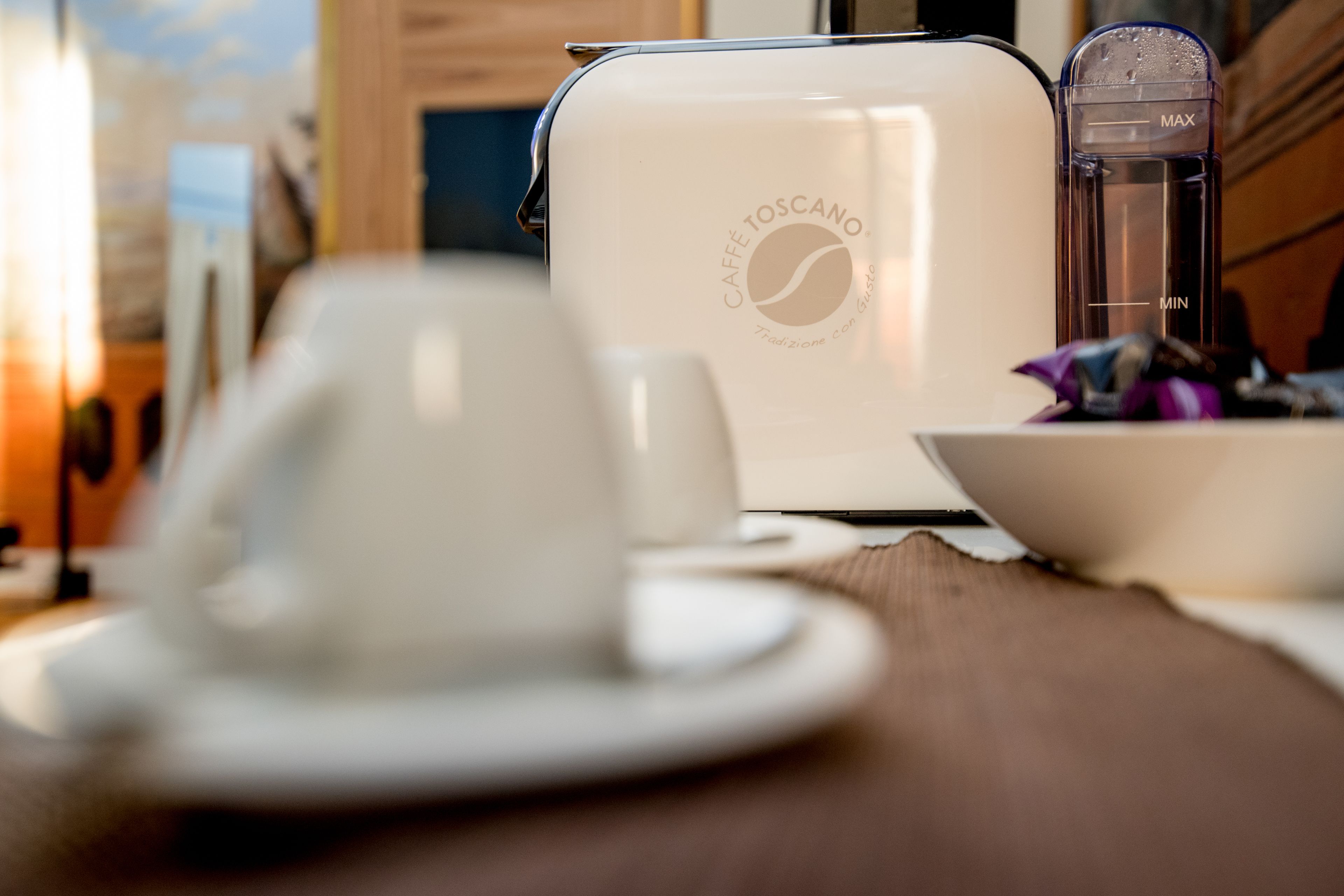 A coffee maker with a cup and saucer on a wooden table.