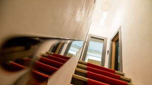 A staircase with red carpeted steps and a wooden handrail. - Dimora Intini (Noci)