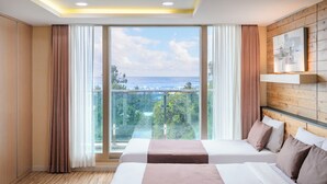 Habitación de hotel con dos camas, un ventanal con vistas al mar y una pared de madera con un estante.