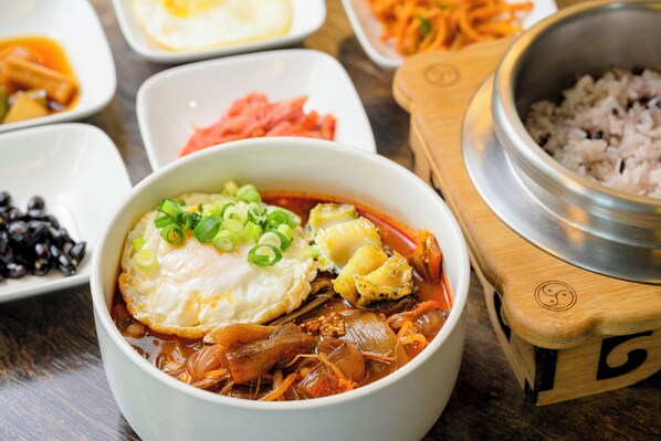 Un tazón de sopa picante con un huevo escalfado, adornado con cebollines, rodeado de guarniciones variadas.