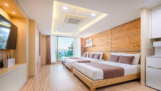 Una habitación de hotel moderna con suelo de madera, dos camas, un televisor y un ventanal con vistas.