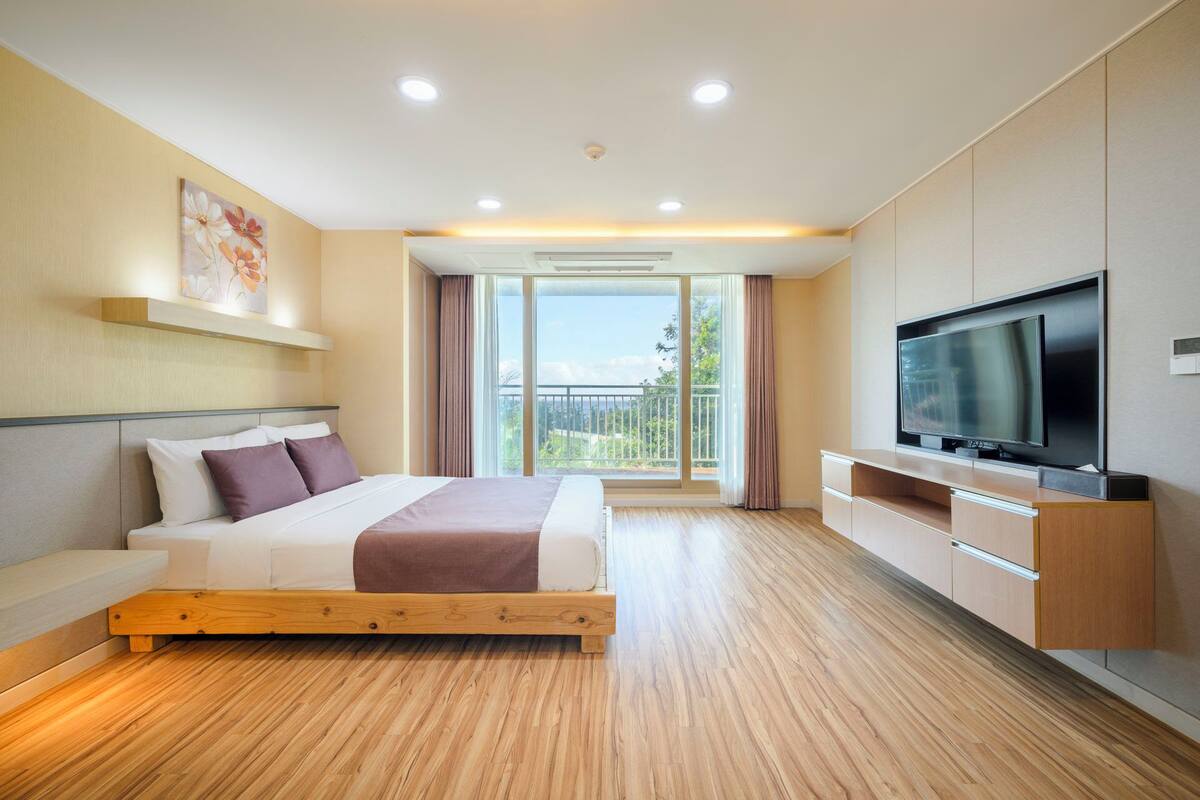 A modern hotel room with a large bed, a flat-screen TV, and a balcony with a view.