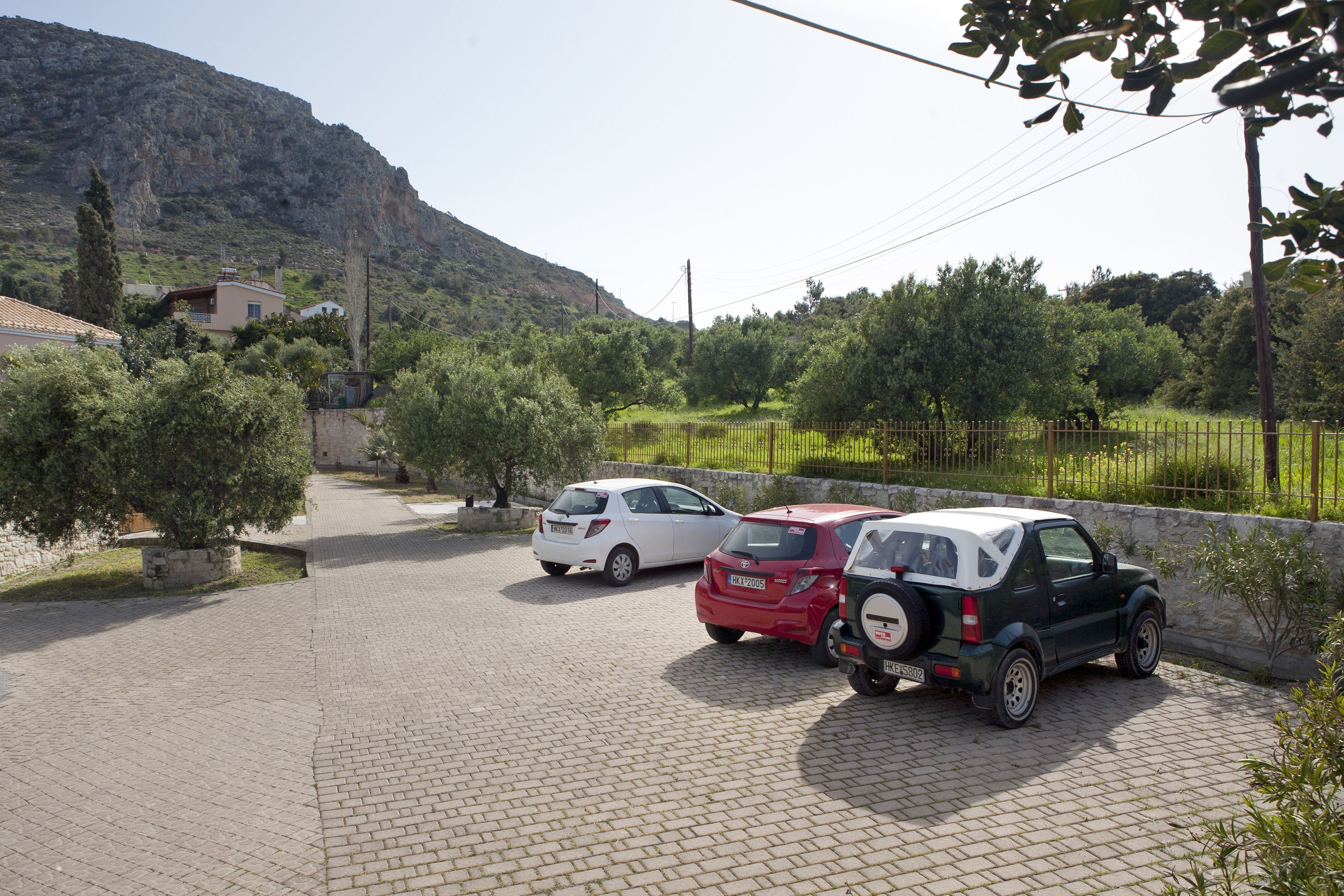 A paved driveway with two parked cars and a stone wall.