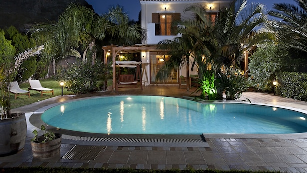 A swimming pool with a patio area, palm trees, and a house with a tiled roof. - Pandora Villas (Hersonissos)