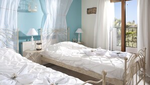 A bedroom with two beds, a window with a view, and a small table with a lamp. - Pandora Villas (Hersonissos)