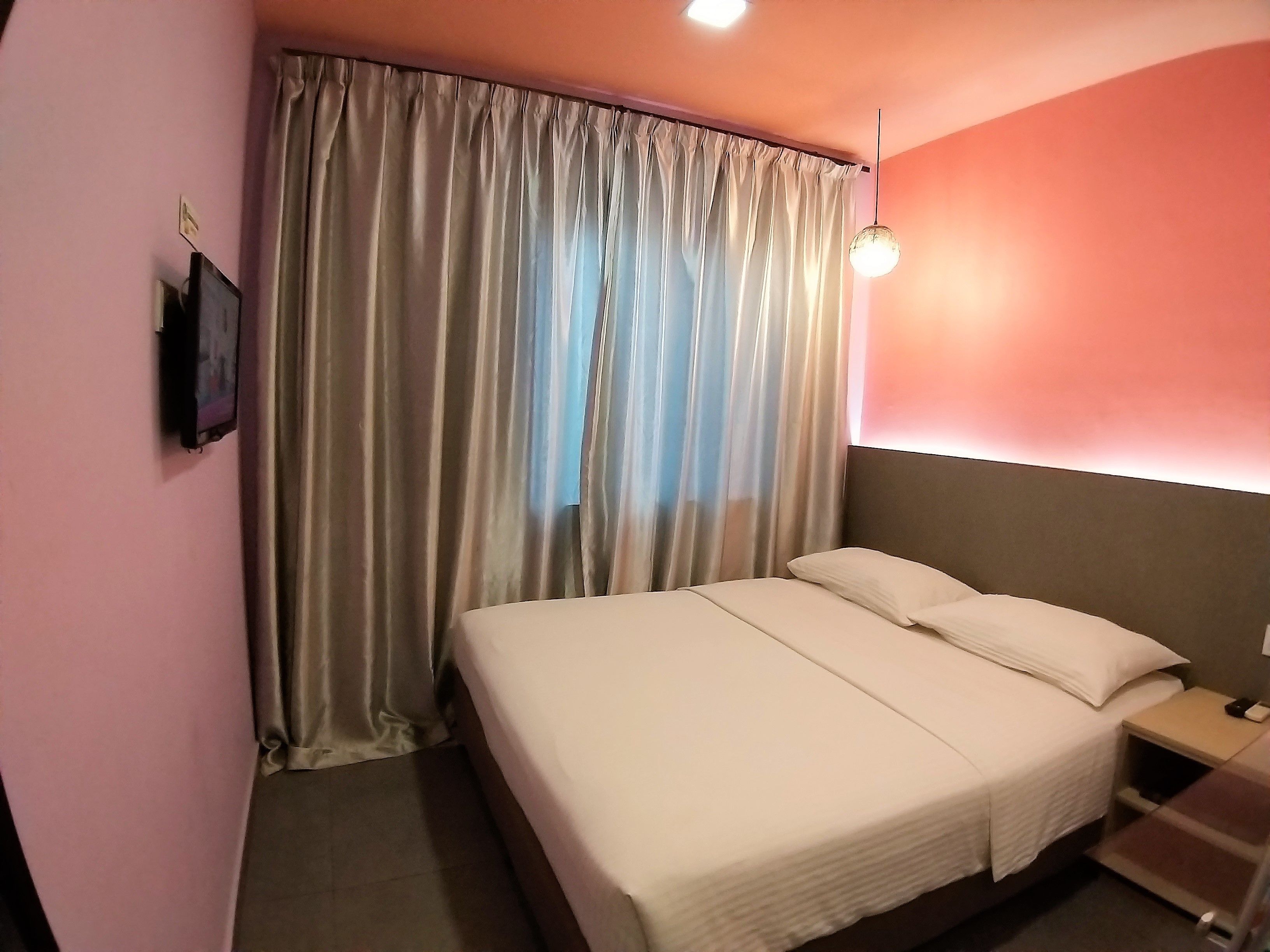A hotel room with a bed, curtains, a nightstand, and a wall-mounted TV.