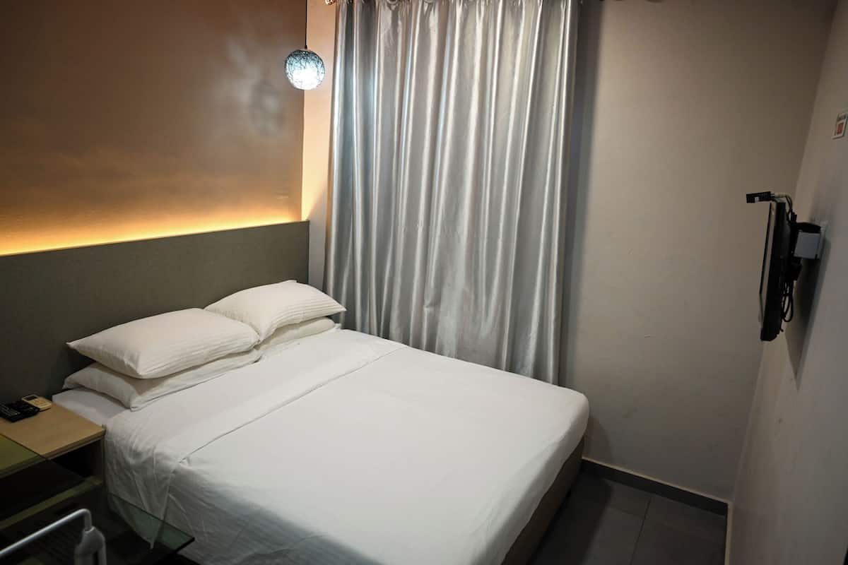 Una habitación de hotel con una cama, una mesita de noche con un teléfono, una lámpara y una cortina.