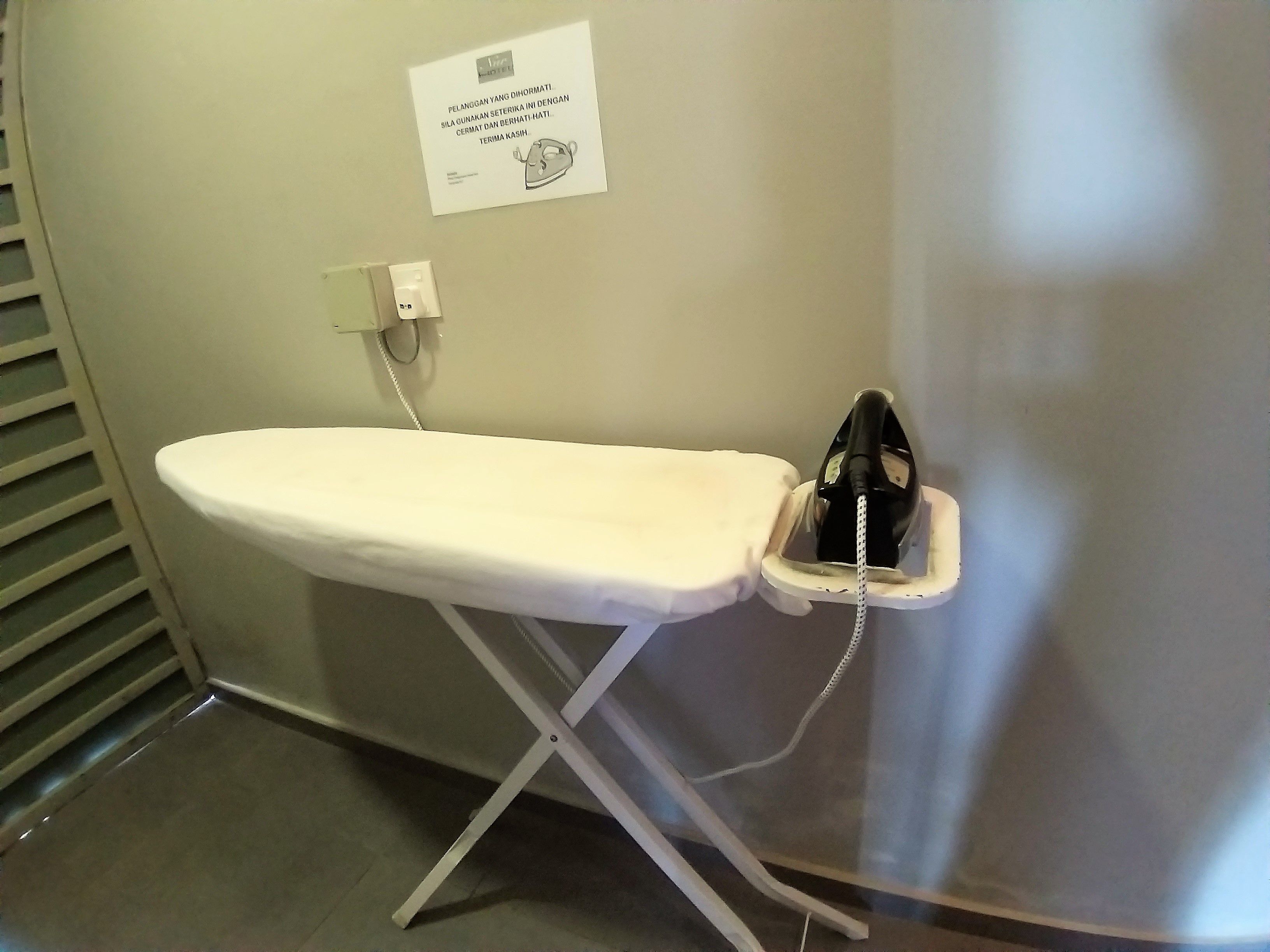 A white ironing board with an iron in a corner, a wall-mounted phone, and a sign with text.