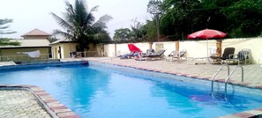 A swimming pool with lounge chairs and umbrellas, surrounded by a brick walkway and palm trees.