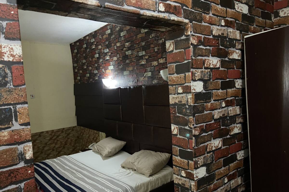Une chambre avec une tête de lit ornée d’un motif en briques, un lit avec une literie à rayures et un mur uni.