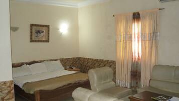 A hotel room with a bed, two chairs, a small table, and a curtain.