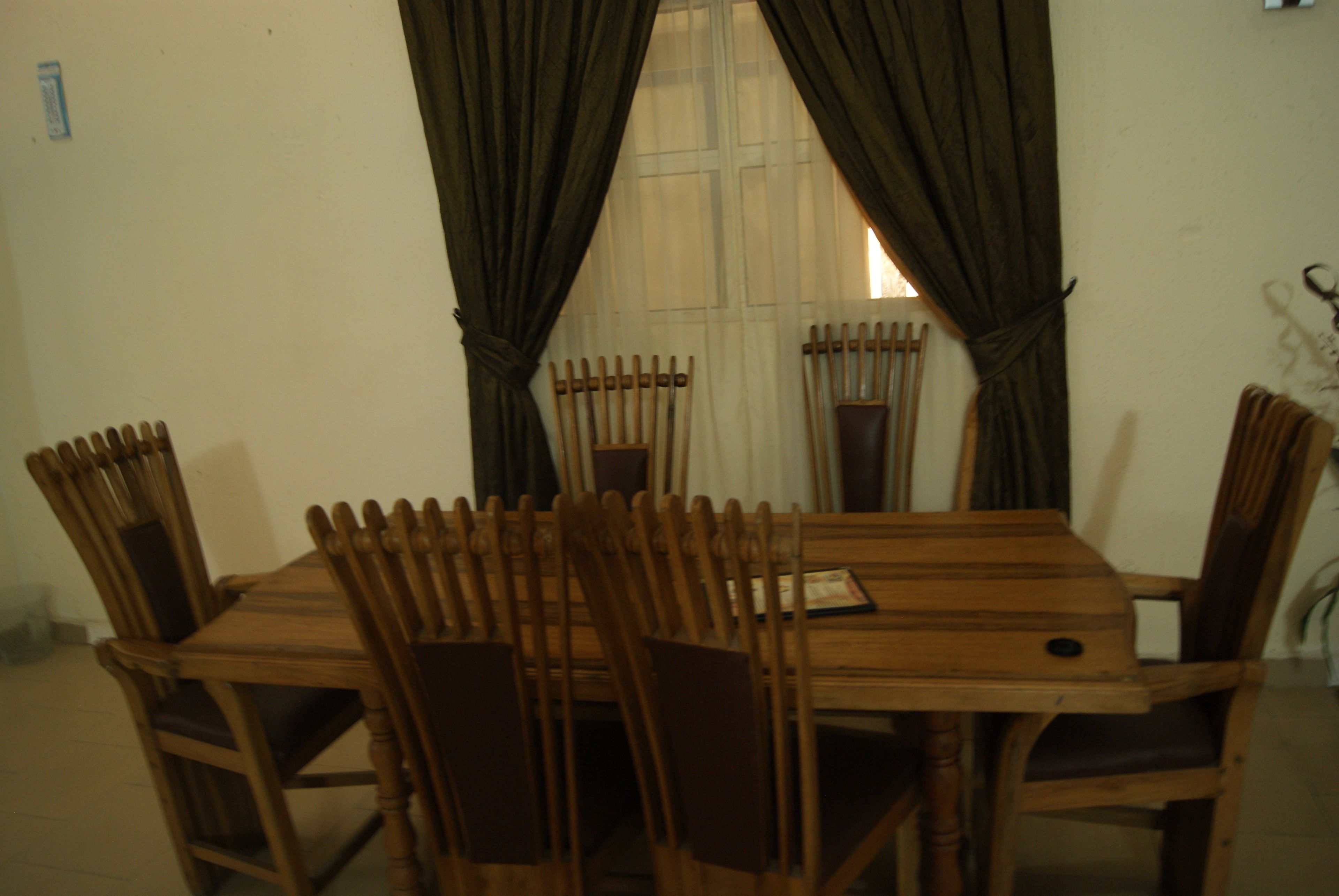 A dining area with a wooden table and chairs, a window with curtains, and a wall-mounted light fixture.