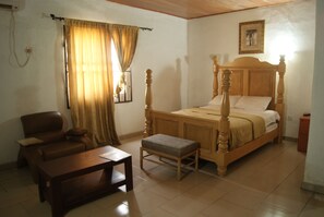 A bedroom with a wooden four-poster bed, a wooden nightstand, a wooden bench, a wooden chair, and a small table.