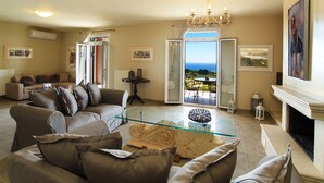 A living room with a glass coffee table, a fireplace, and a view of the outdoors. - Liogerma Vacation Home (Kefalonia)