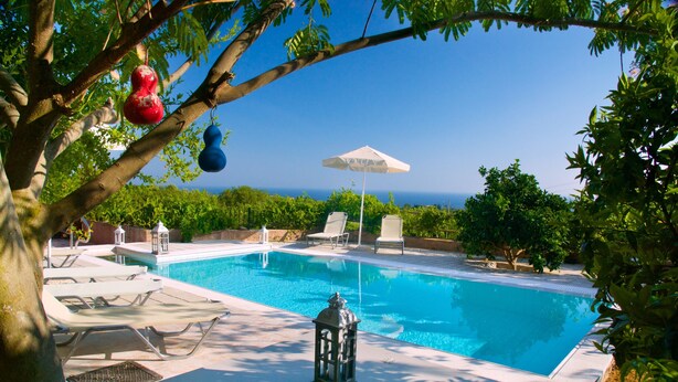 A swimming pool with lounge chairs and a lantern, surrounded by greenery and a clear view of the ocean. - Liogerma Vacation Home (Kefalonia)
