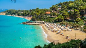 A beach with clear turquoise waters, sun loungers, umbrellas, and a building with a terrace overlooking the sea. - Liogerma Vacation Home (Kefalonia)