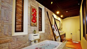 A bathroom with a stone wall, a bathtub with rose petals, a wooden ladder, and a yellow wall. - The Kara Pool Villa (Sa Khu)