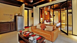 A modern living room with a sofa, a coffee table with fruits and magazines, a refrigerator, and a kitchen area with a sink and cabinets. - The Kara Pool Villa (Sa Khu)