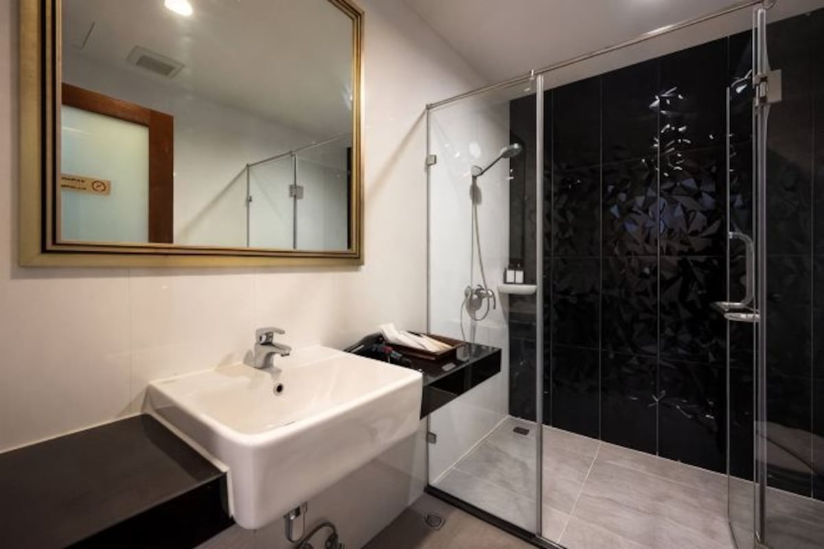 Un baño moderno con un lavabo blanco, un espejo grande y una ducha con cerramiento de vidrio.