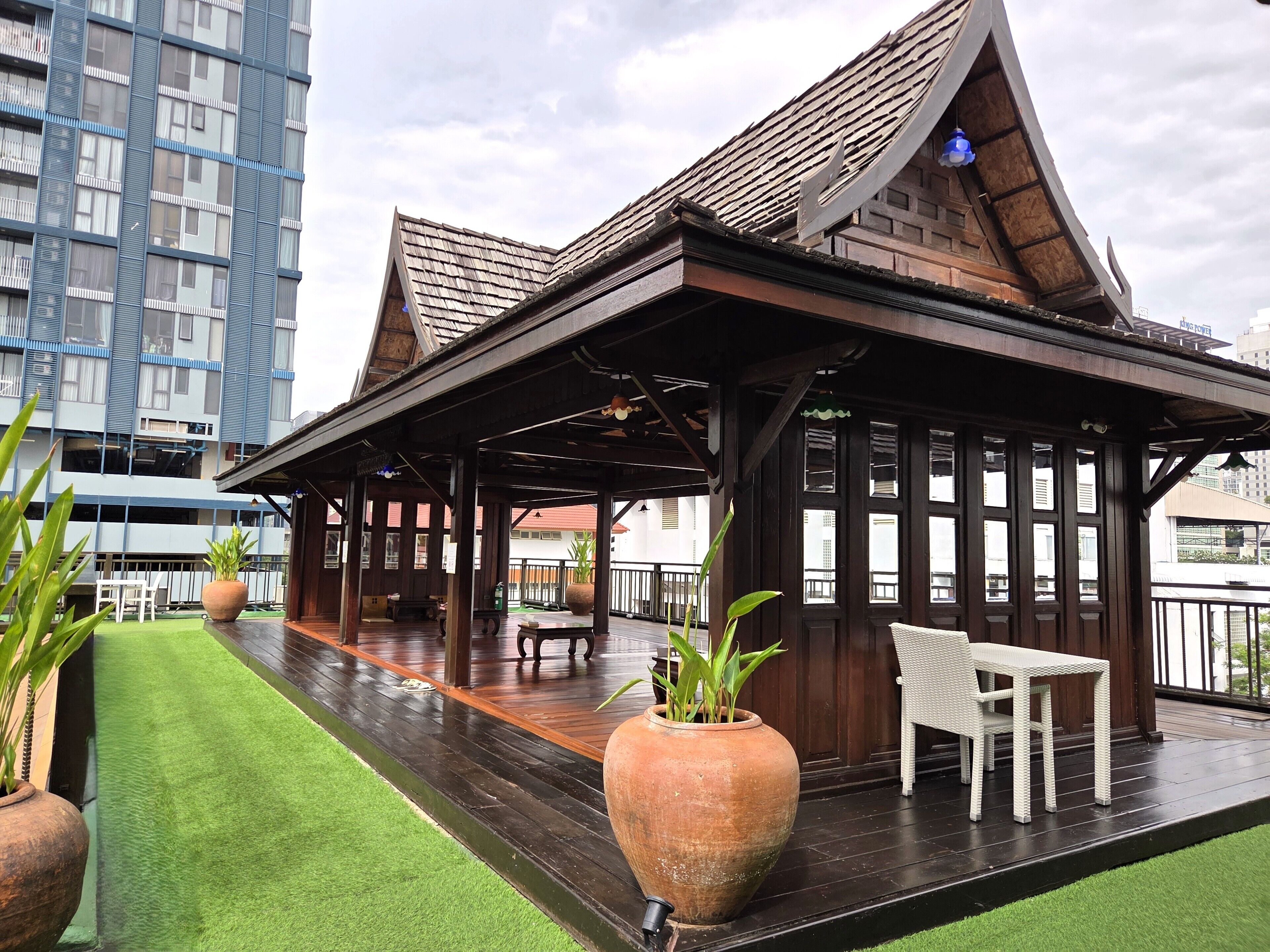 Un espacio al aire libre techado con terraza de madera, plantas en macetas y un área de estar.