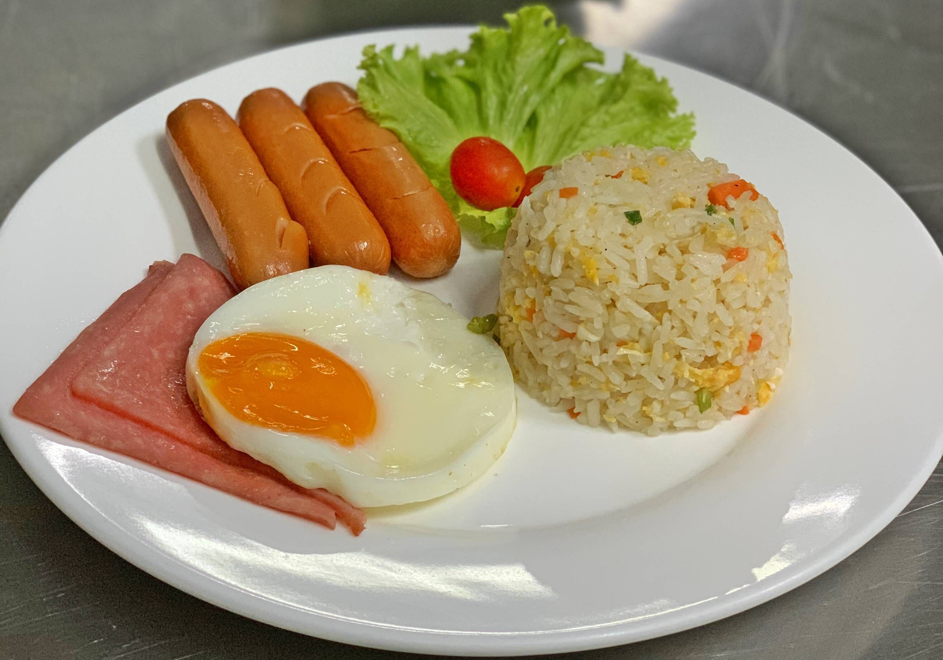 A plate with fried rice, three sausages, a fried egg, and some lettuce.