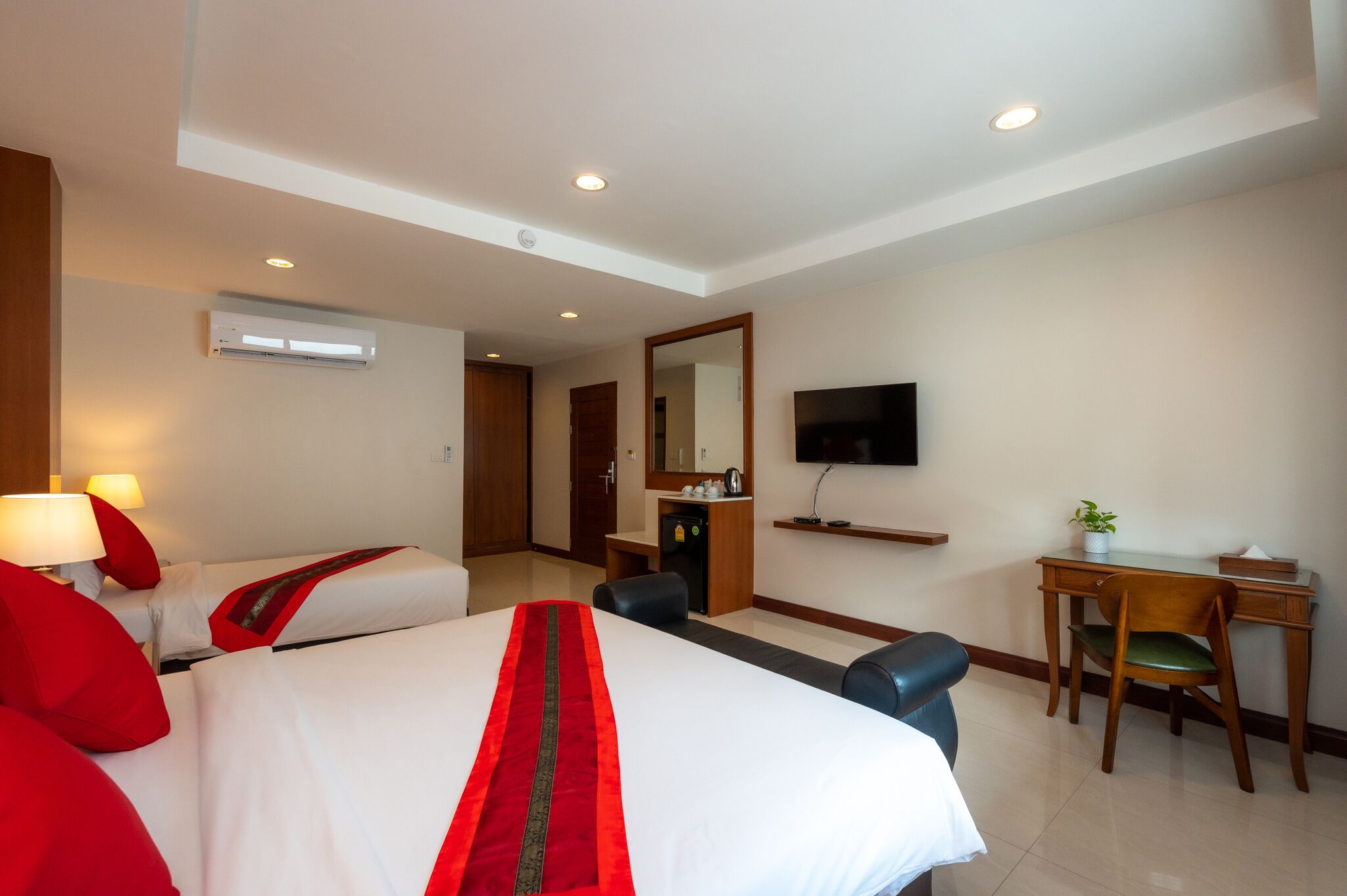 A hotel room with two beds, a desk, a chair, a TV, and an air conditioning unit.